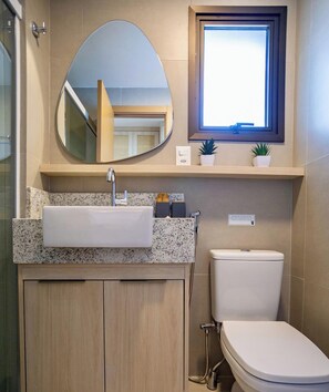 A bathroom with a sink, mirror, toilet, and a window above the sink.