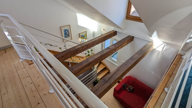 Una habitació amb sostre alçat, una escala de fusta, un sofà vermell i vista cap a l'exterior.