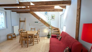 Una habitació amb taula i cadires de fusta, un sofà vermell, una escala i una planta en test.