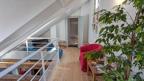 Un dormitori tipus loft amb sostre inclinat, un llit superposat, una cadira vermella i una taula de fusta amb llibres.