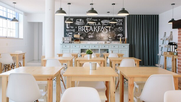 A modern dining area with wooden tables and white chairs, a chalkboard menu, and pendant lighting. - Zulla Nazaré Surf Village  (Nazaré)