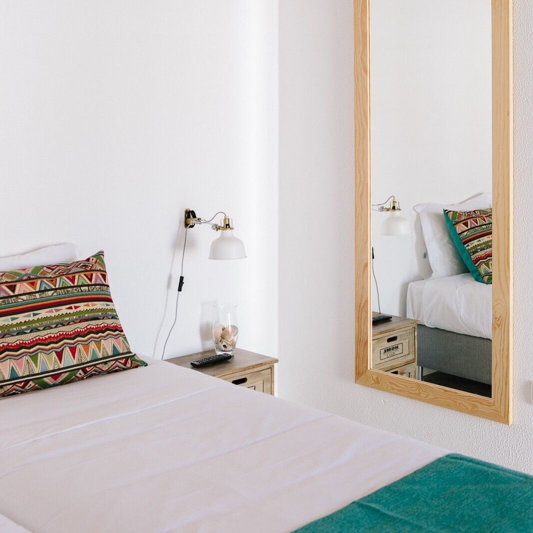 Habitación de hotel ordenada con cama, mesita de noche, lámpara y espejo.