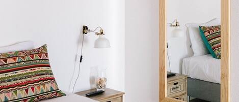 A neatly arranged hotel room with a bed, a bedside table, a lamp, and a mirror.