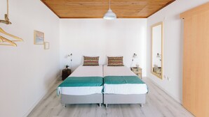 A double bed with two pillows, a bedside table with a lamp, a hanging light fixture, and a wooden door. - Zulla Nazaré Surf Village  (Nazaré)