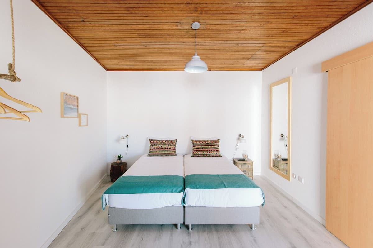 Un lit double avec deux oreillers, une table de chevet avec une lampe, un luminaire suspendu et une porte en bois.