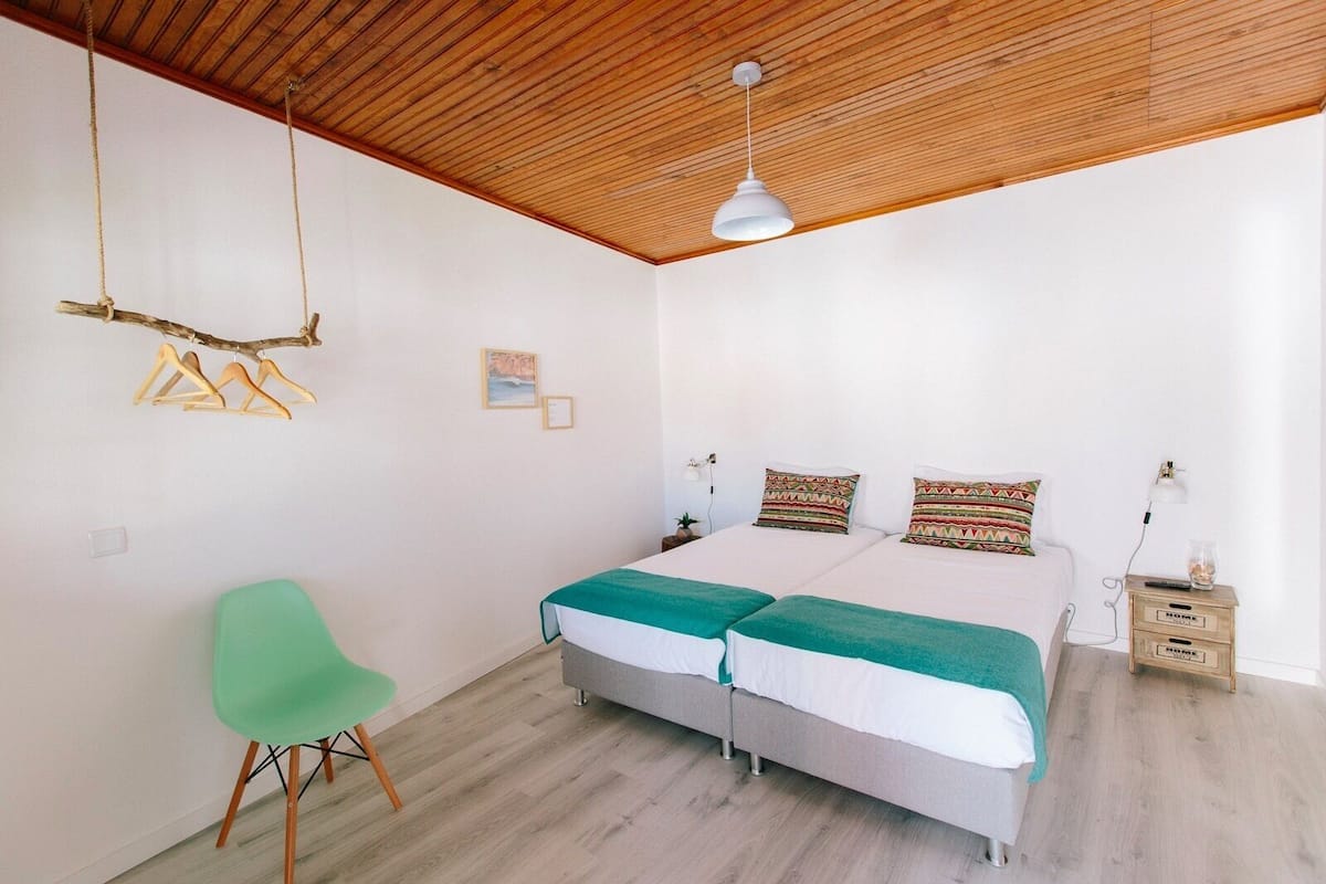 Une chambre avec un plafond en bois, un lit avec deux oreillers, une chaise verte et une table de chevet avec une lampe.