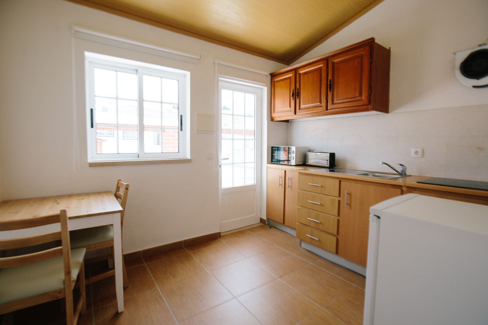 A small kitchen with wooden cabinets, a microwave, a sink, and a refrigerator.