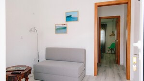 A small, modern room with a grey sofa, a wooden side table, and two framed pictures on the wall. - Zulla Nazaré Surf Village  (Nazaré)