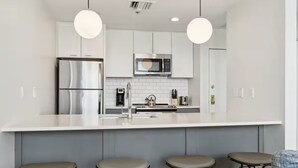 A modern kitchen with a stainless steel refrigerator, a microwave, and a kettle on the counter. There are four stools under the counter. - Union Station Stay | Spacious Unit w/ Kitchen | Walk to Parks & Museums (Pittsburgh)