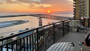 Ein Balkon mit Blick auf einen Sonnenuntergang über einem Fluss, einen Steg und ein Gebäude mit Balkonen.
