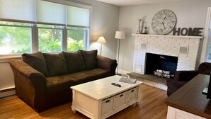 A living room with a brown couch, a white coffee table, a fireplace, and a clock on the wall. - Marvelous 4-bedroom, 2-bath home with AC and private backyard close to the beach (Narragansett)