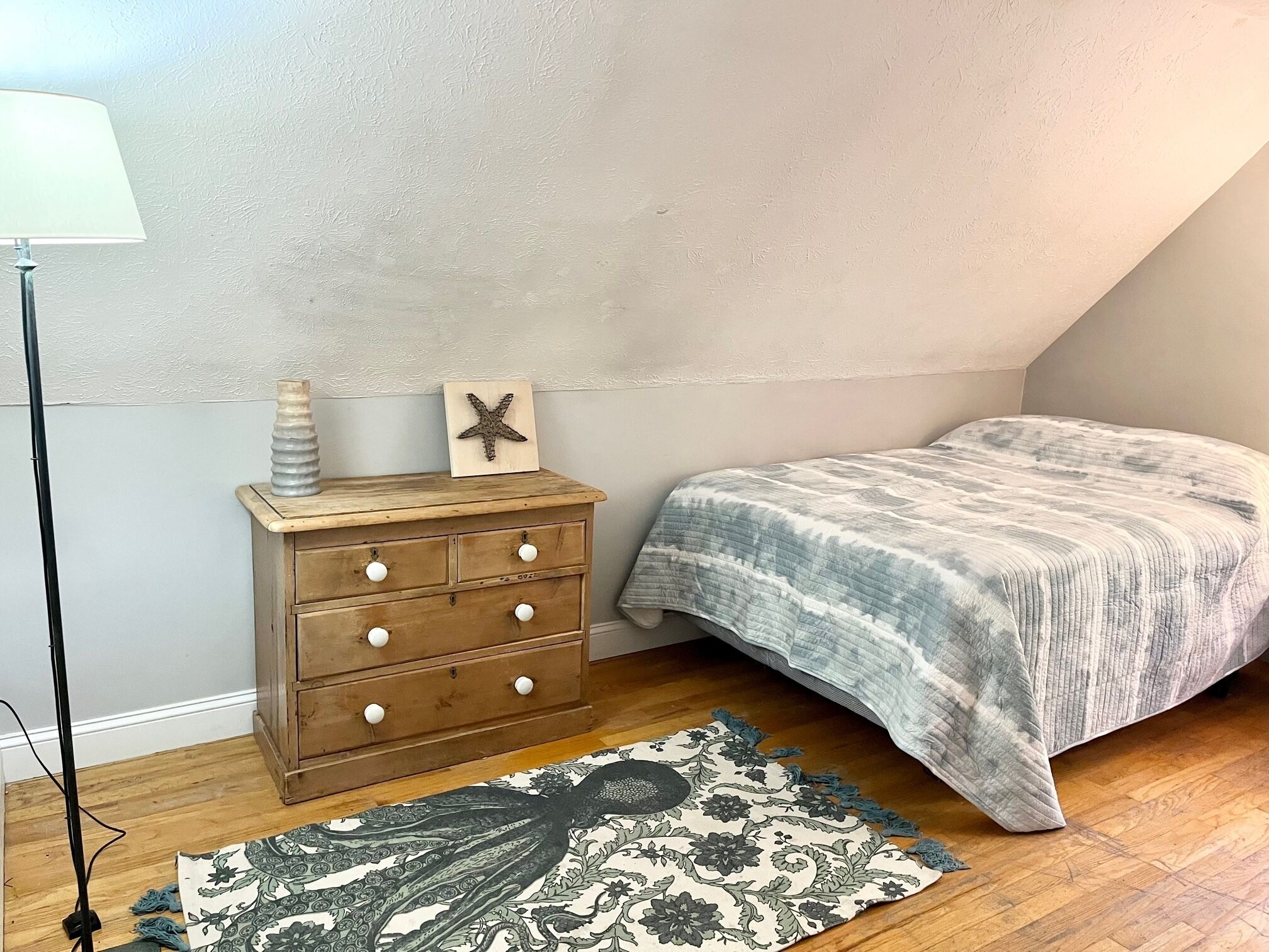 A bedroom with a wooden dresser, a bed with a patterned blanket, a starfish decoration, and a patterned rug.