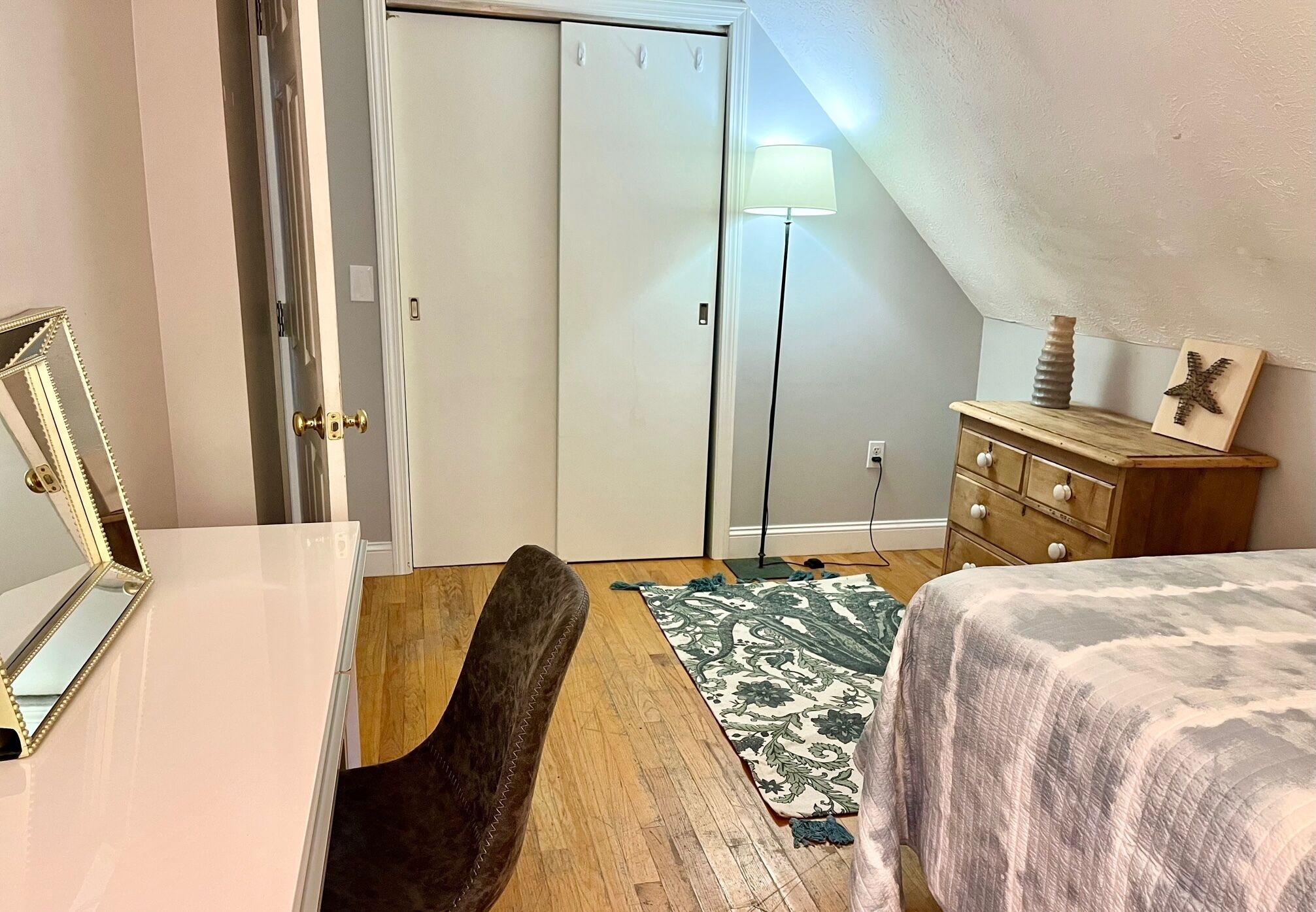 A bedroom with a bed, a dresser, a mirror, a door, a lamp, and a rug.