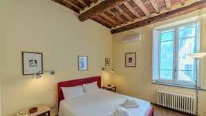 A hotel room with a bed, bedside tables, framed pictures, a window with a view, and a radiator.