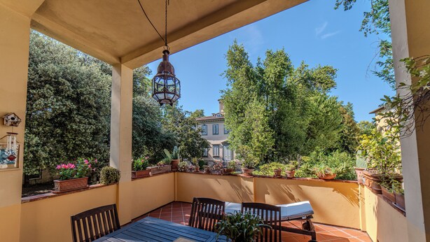 A covered patio with a table, chairs, and potted plants.
