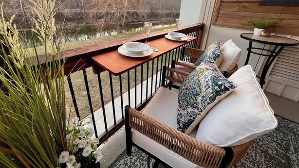 A patio with a wooden table set for two, wicker chairs, and a cushioned bench with patterned pillows. - Fox Trail Hideaway by Branson Landing-Waterfront (Branson)