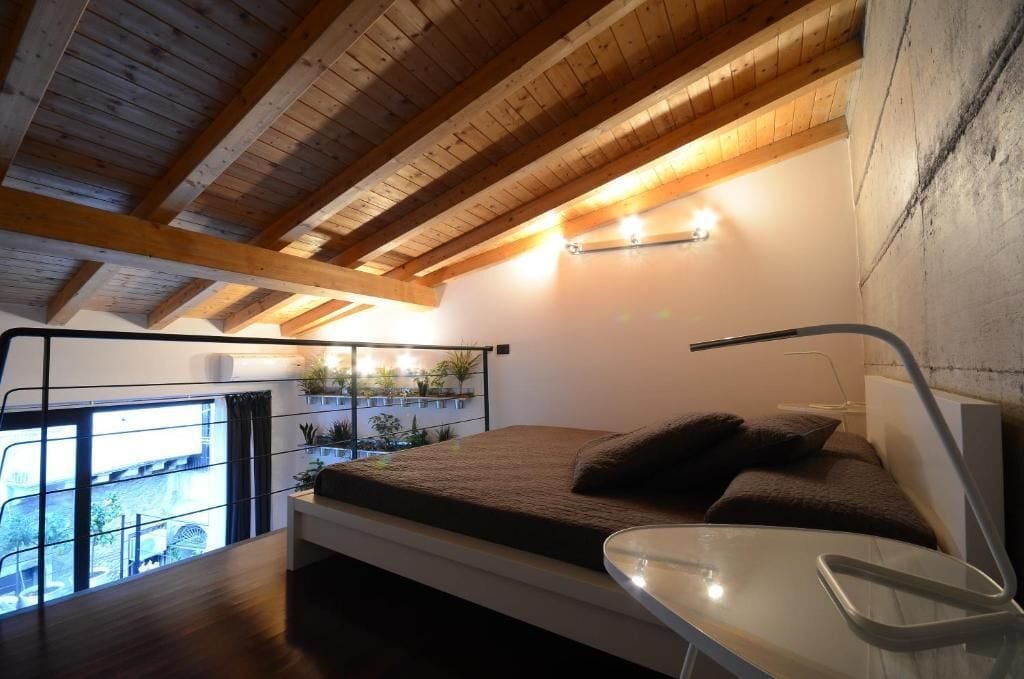 A modern bedroom with a sloped ceiling, a bed with a headboard, a bedside table, and a view of the outdoors.