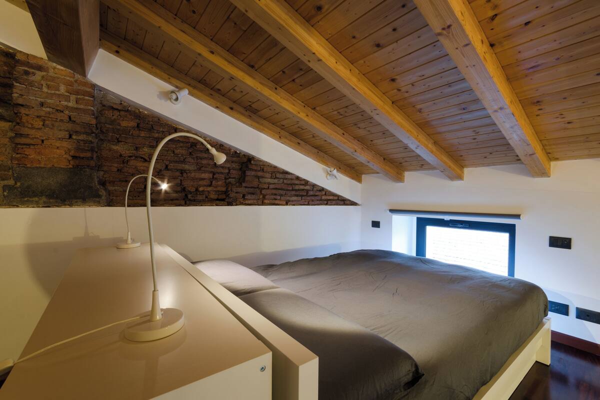 A bedroom with a sloped ceiling, exposed brick wall, and a large window.