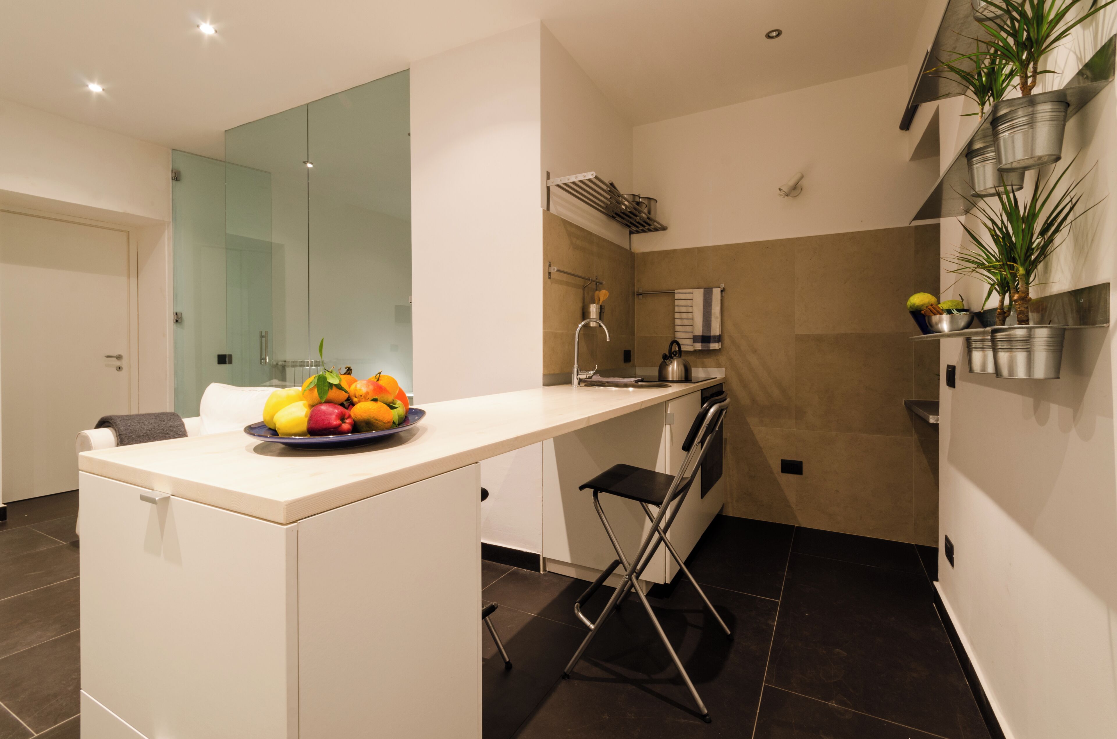 Eine moderne Küche mit weißer Arbeitsplatte, Obstschale, Wasserkocher und klappbarem Stuhl.