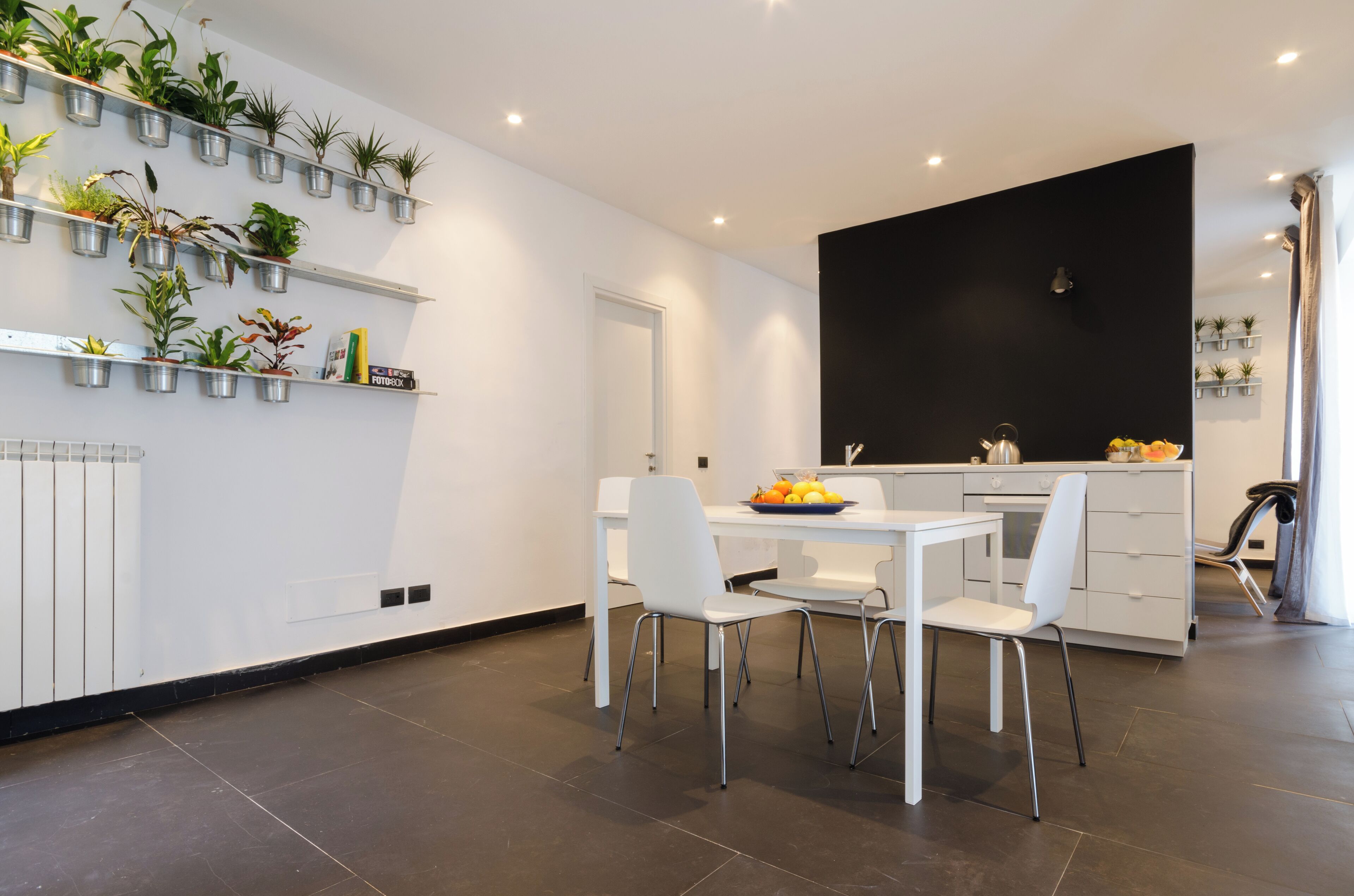 A modern kitchen with white cabinetry, a black accent wall, and a dining area with white chairs and a table.
