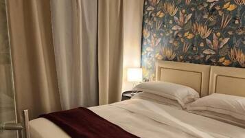 Habitación de hotel con cama, cortinas, mesita de noche y un papel tapiz floral.
