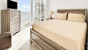 A bedroom with a large bed, a wooden dresser, a television, and a window with a view of a building. - Luxurious 2BD Condo with Direct Ocean Views & Resort Pool - Apartment (Sunny Isles Beach)