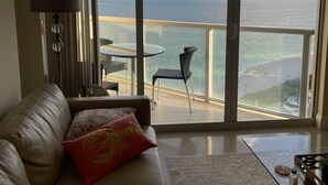 A hotel room with a balcony overlooking the sea, a sofa, a table, and a lamp. - Luxurious 2BD Condo with Direct Ocean Views & Resort Pool - Apartment (Sunny Isles Beach)