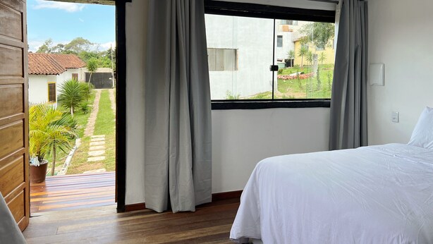 A bedroom with a bed, a window with curtains, and a view of the outside. - Pousada Villa Salgueiro (Ouro Preto)