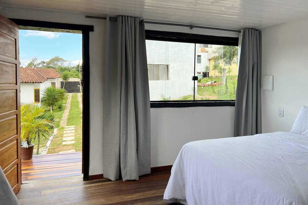 A bedroom with a bed, a window with curtains, and a view of the outside.