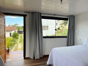 Ein Schlafzimmer mit Bett, einem Fenster mit Vorhängen und Blick ins Freie.
