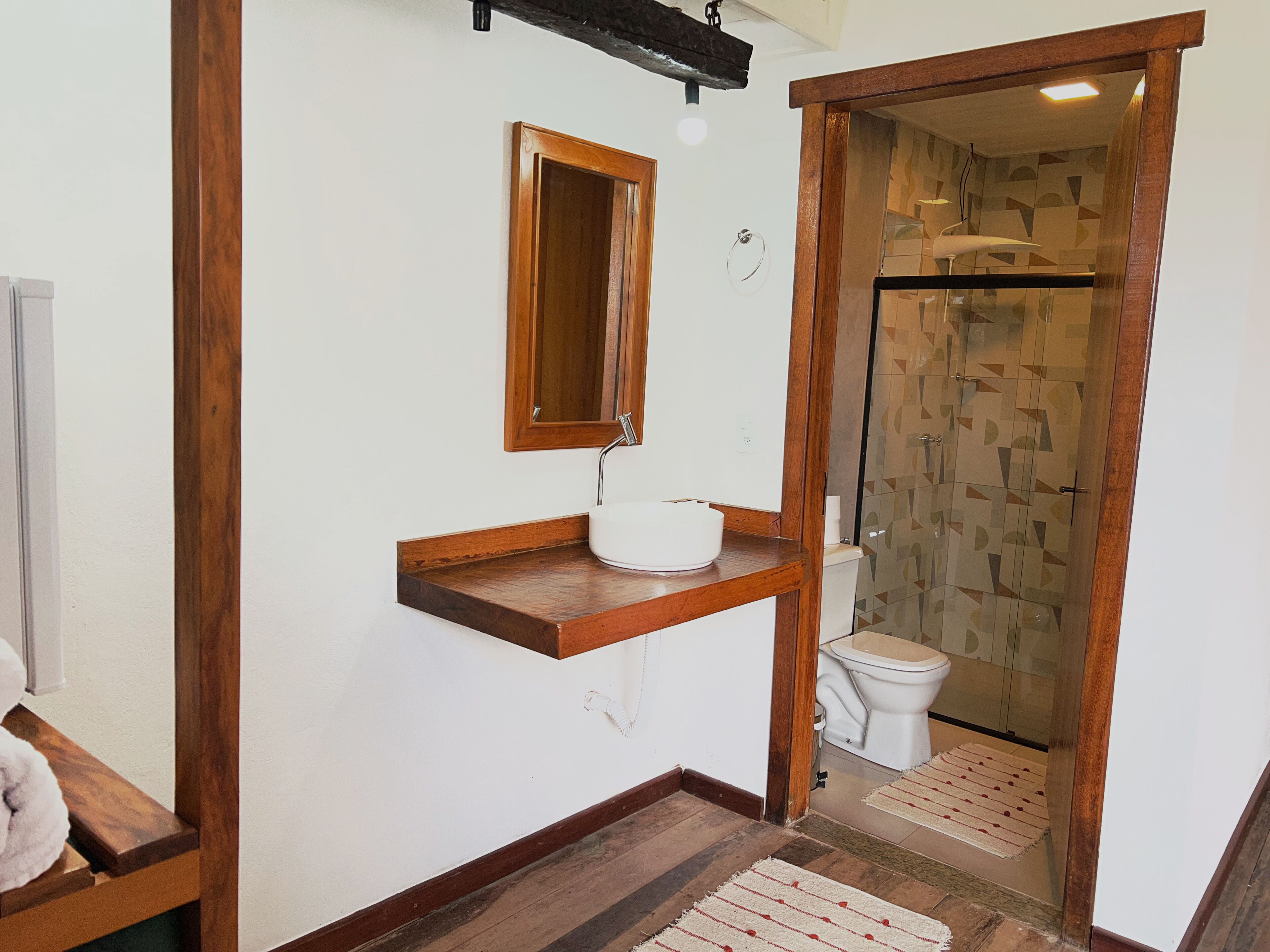 Uma casa de banho com toucador de madeira, espelho, sanita e cabine de duche com azulejos estampados.