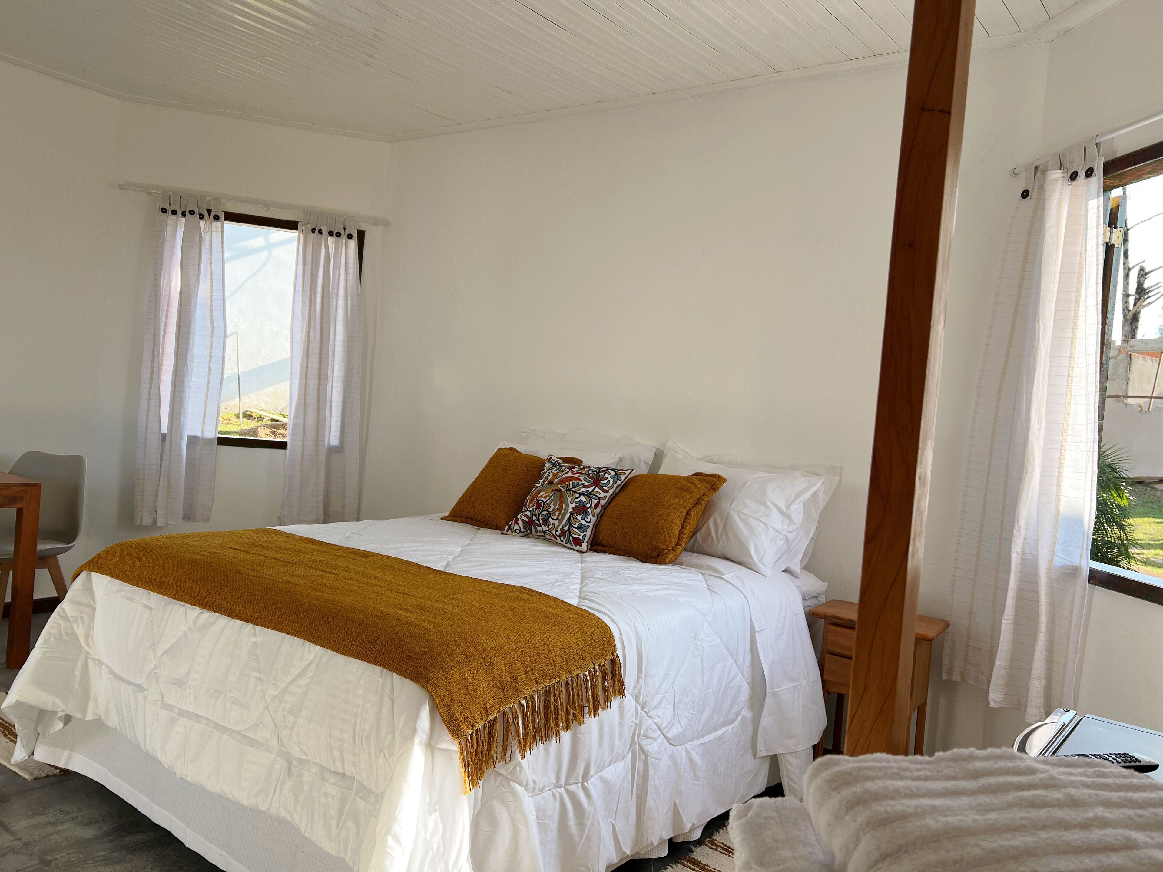 A neatly made bed with a white comforter and a brown throw blanket, a wooden nightstand, and a small table with a lamp.