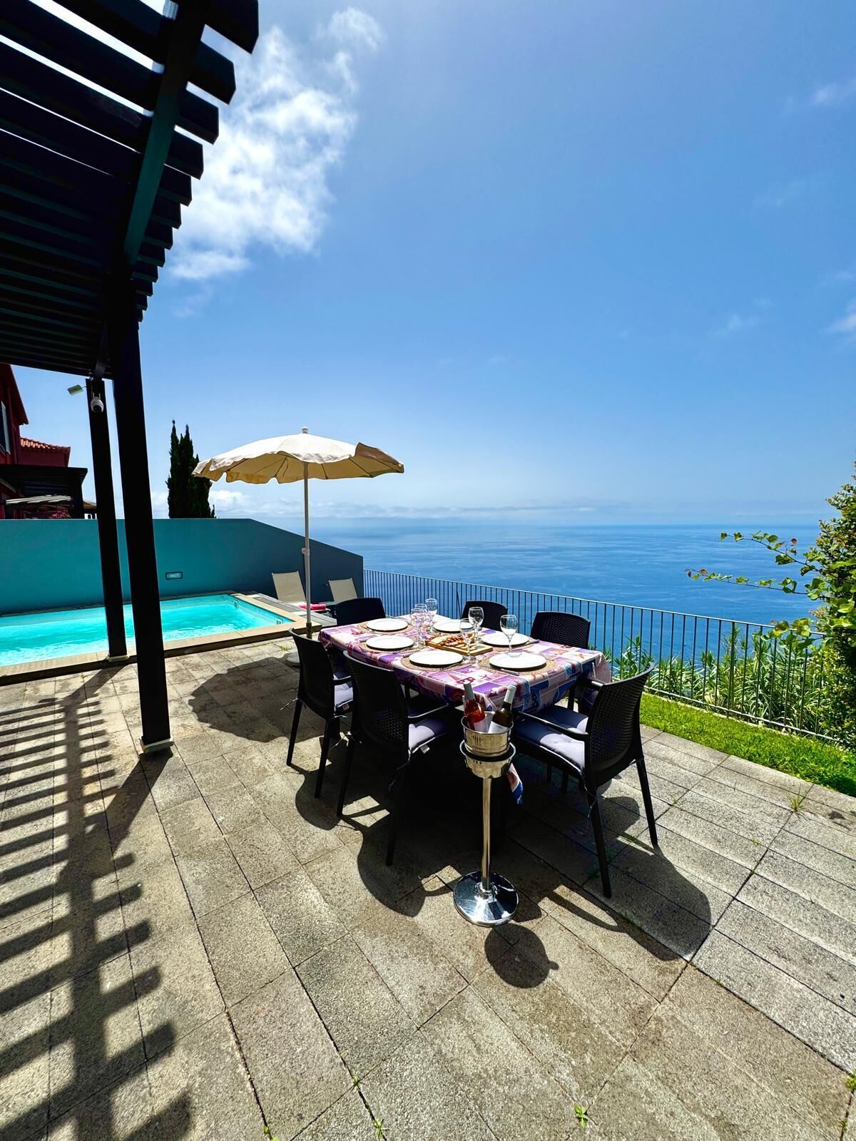 Uma área de refeições ao ar livre com uma mesa posta para quatro pessoas, com vista para uma piscina e o mar.