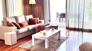 Un salon moderne avec un canapé, une table basse et une lampe. On aperçoit un balcon avec des chaises.