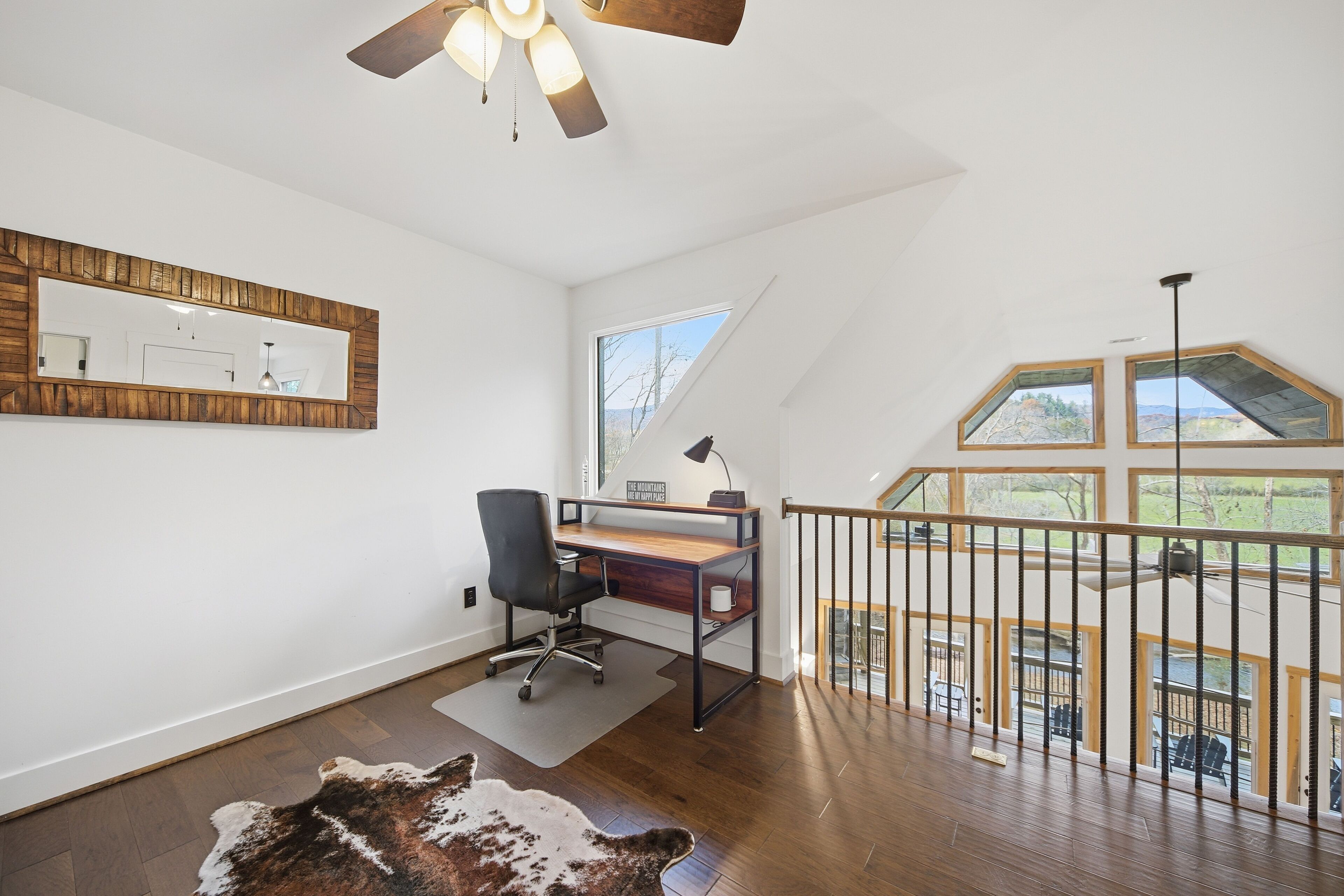 A spacious room with a wooden desk, a black office chair, a large mirror, and a wooden ceiling fan.