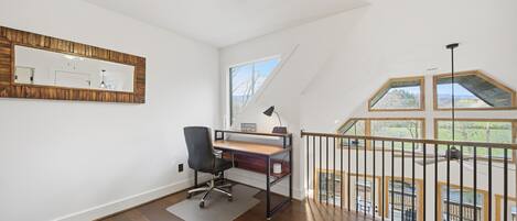 A spacious room with a wooden desk, a black office chair, a large mirror, and a wooden ceiling fan.