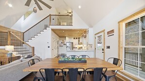 A spacious dining area with a wooden table and chairs, a staircase leading to an upper level, and a view of the kitchen and living area. - Creeks n' Peaks - Ellijay, GA (Ellijay)