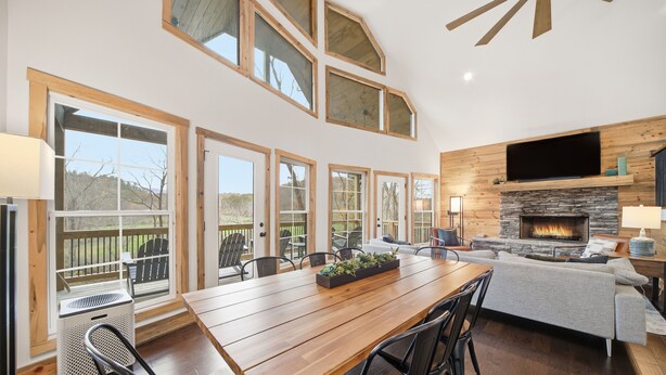 A spacious dining area with a wooden table and chairs, a fireplace, and a large TV mounted on the wall. - Creeks n' Peaks - Ellijay, GA (Ellijay)