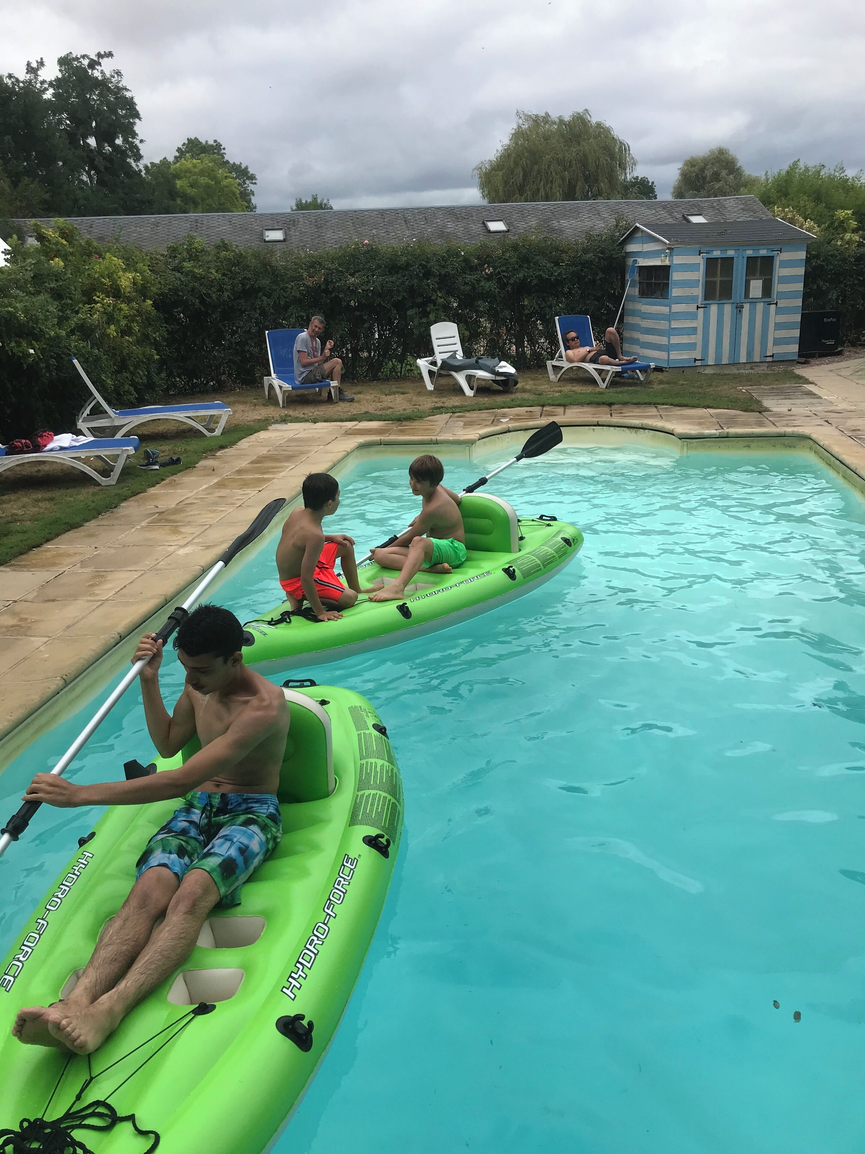 Une piscine où deux personnes sont à bord de kayaks gonflables verts.