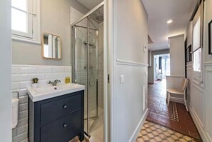 A modern bathroom with a glass shower enclosure, a white sink, and dark cabinetry. - Spacious 4-Bedroom Apartment in Eixample – Perfect for Families & Longer Stays (Barcelona)
