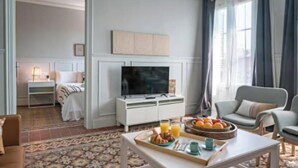 Ein Hotelzimmer mit Bett, Fernseher, Esstisch mit Frühstück und einer Couch.