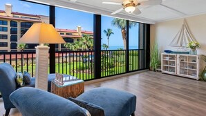 Un balcón amplio con vista al océano, ventilador de techo y zona de estar con lámpara y mueble.