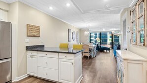 Una cocina amplia con una isla central, armarios blancos y un comedor con sofá azul y sillas amarillas.