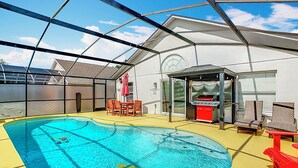 An indoor swimming pool with a covered patio area, a barbecue station, and outdoor seating.
