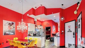 A modern kitchen with red walls, a dining area with yellow chairs, and a chandelier.