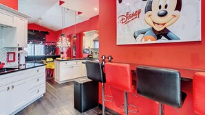 A modern kitchen with white cabinets, a black countertop, and a Mickey Mouse poster on the wall.