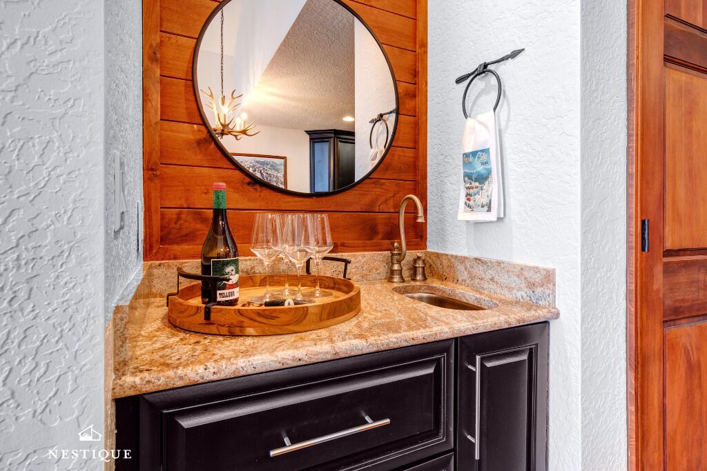 A kitchen with a wooden backsplash, a round mirror, a wine bottle, and glasses on a wooden tray.