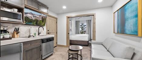 A modern kitchen with stainless steel appliances, a dining area with a white table and sofa, and a large window with a mountain view.