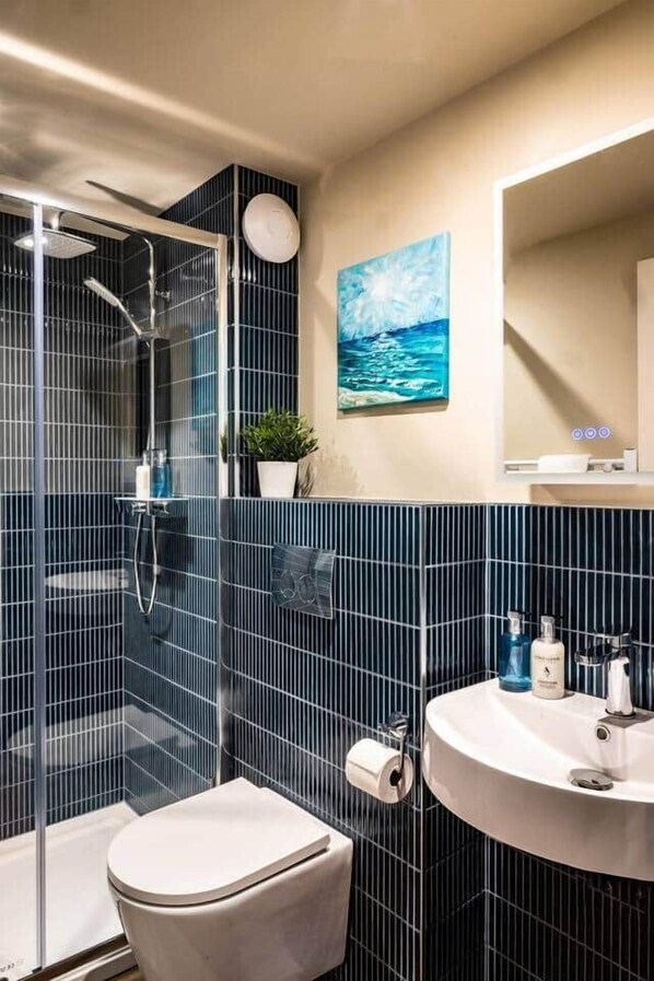 A modern bathroom with a glass-enclosed shower, a toilet, and a sink with toiletries.