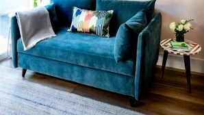 Una sala de estar moderna con un sofá color turquesa, un espejo decorativo y una pequeña mesa redonda con un jarrón de flores.